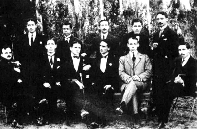 Fotografía grupal de jóvenes de terno en un jardín, unos sentados y otros de pie